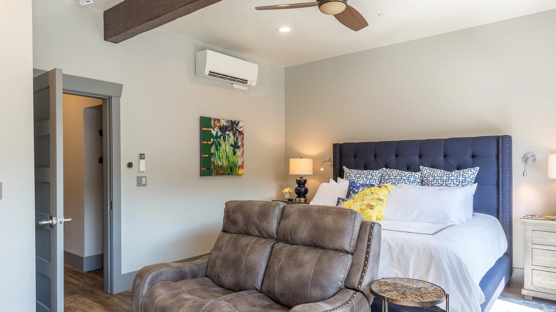 A bedroom with a welcoming bed, broad brown colored chair and comforter and a ceiling fan above
