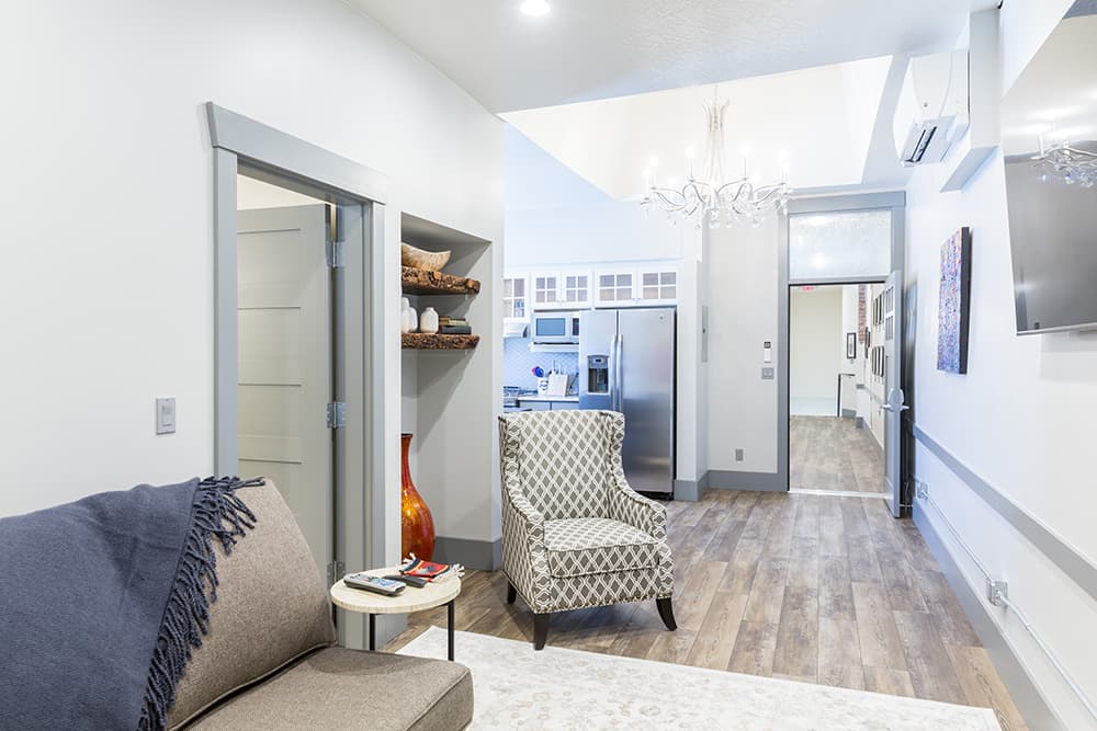 Modern armchair in a sitting area looking down a hallway to a kitchen and stairway.